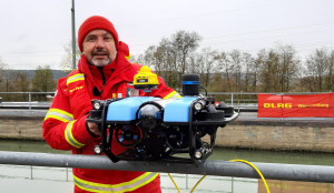 Projektleiter Dr. Thorsten Lück zeigt eine Unterwasserdrohne (blau) mit aufgesetztem Navi (gelb) am Main-Donau-Kanal. Foto: Claire Girard, DLRG 